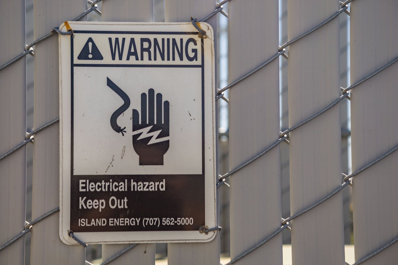 Home Close-up of a warning sign for electrical hazards on a chain-link fence.