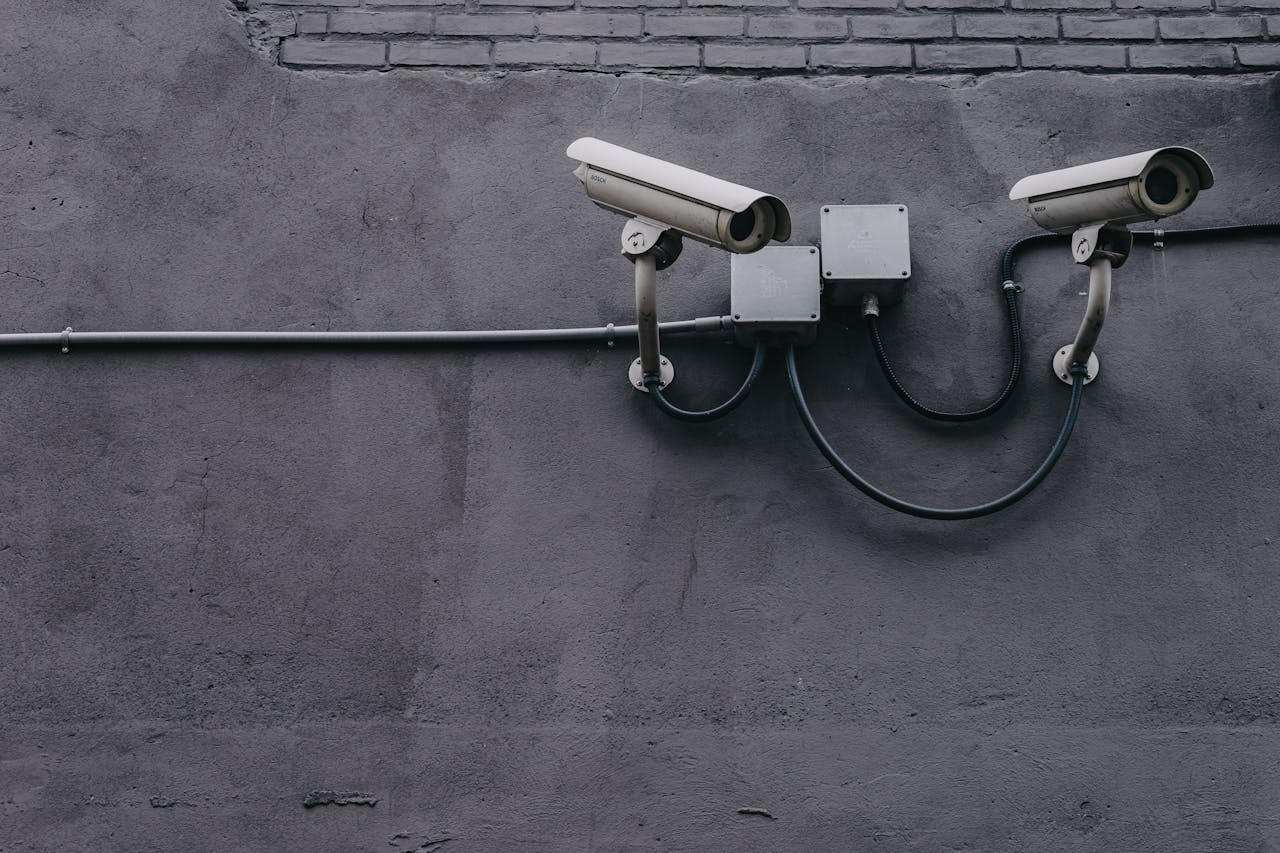 Offerings Two surveillance cameras mounted on a concrete wall, highlighting security technology.